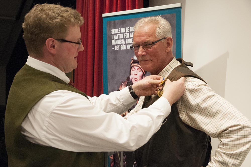 Nytillträdde ordförande för Jägareförbundet Kronoberg Frederik Kjellson kragslår sin företrädare Lennart Haraldsson med länsförbundets förtjänstmedalj i guld. Foto: Jan Henricson